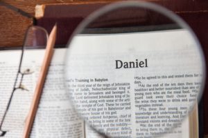 Bible with magnifying glass highlighting title page of Daniel
