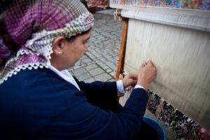 Woman in traditional garb weaving carpet on loom