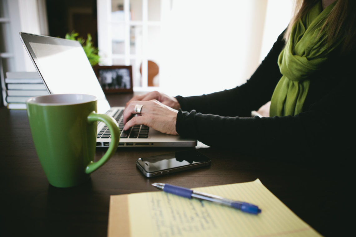 Image of woman using laptop and a green mug