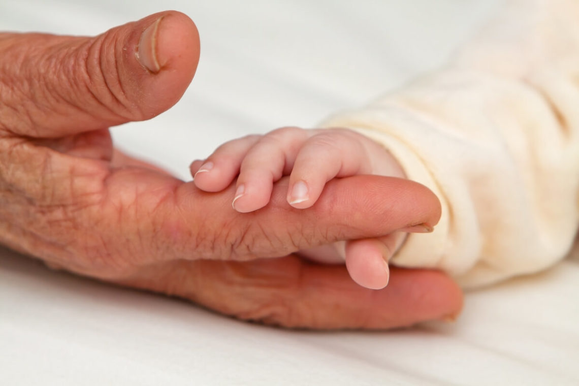 Closeup image of baby holding Great Grandma's fingers