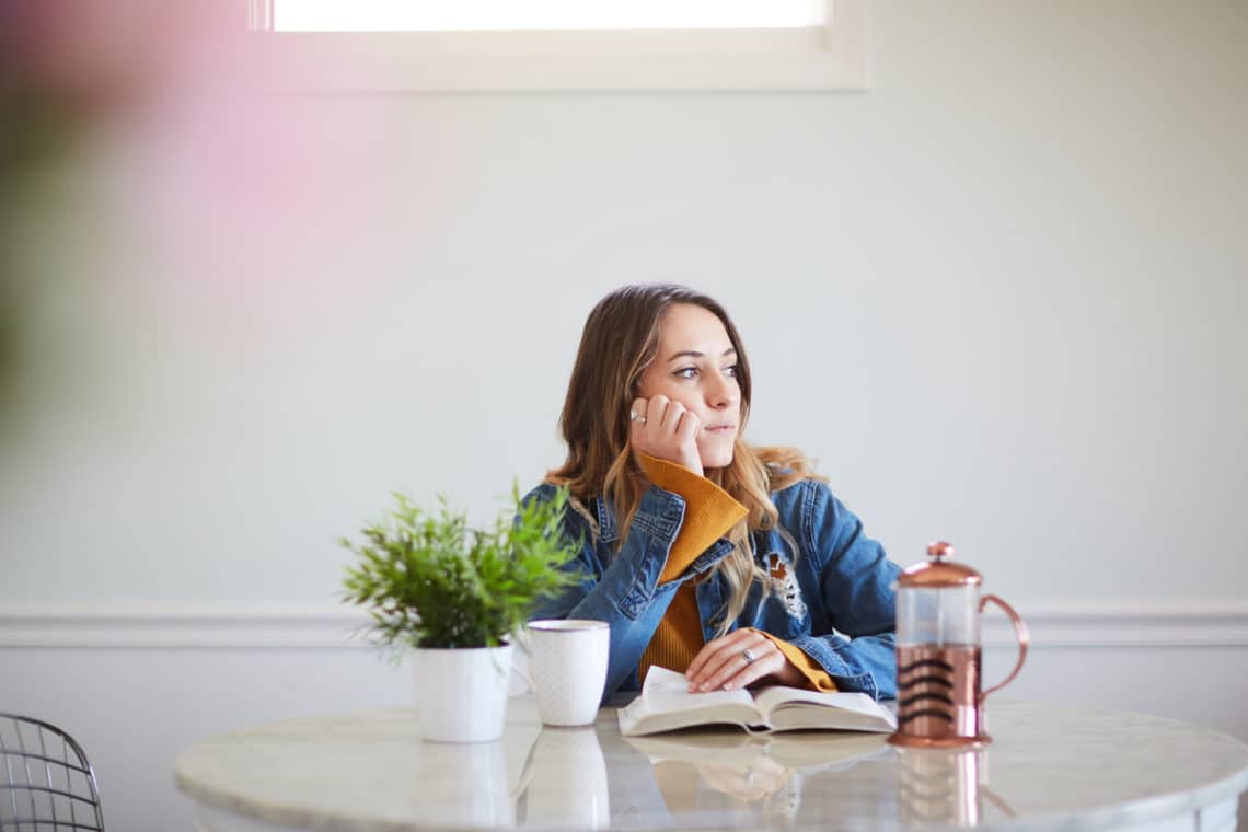 Young woman with open Bible stops to think and gaze out window